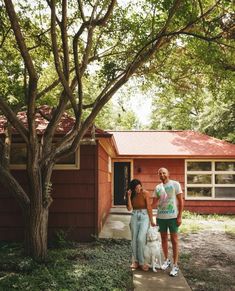 two people standing in front of a red house with a white dog on the sidewalk