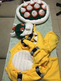 two stuffed animals are laying next to each other on the floor, one is wearing a yellow towel and the other has a green hat