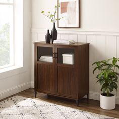 a wooden cabinet with two vases on top of it next to a potted plant