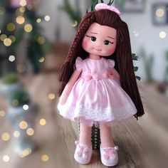 a doll with long brown hair and pink dress sitting on a wooden floor in front of a christmas tree