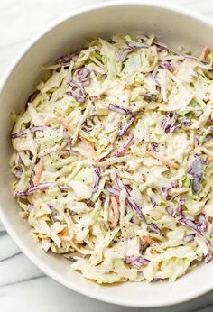 a white bowl filled with coleslaw salad on top of a marble countertop