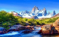 a river running through a lush green forest filled with snow covered mountains in the distance