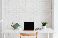 a laptop computer sitting on top of a white desk next to a plant in a vase