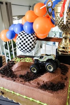 a birthday cake with a monster truck on top and balloons in the air behind it