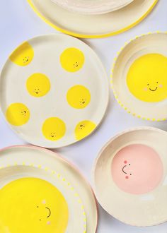 three plates with smiley faces painted on them, one has pink cheeks and the other has yellow eyes