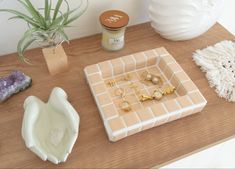 a table topped with different types of jewelry on top of a wooden table next to a potted plant