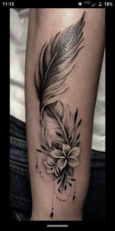 a black and white photo of a feather with flowers on the leg, done by tattoo artist