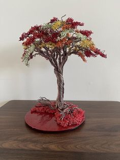 a bonsai tree on a wooden table with red base and roots growing out of it