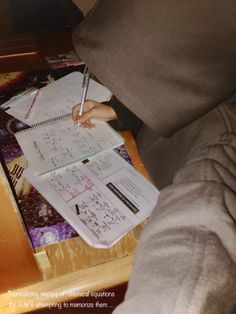 a person sitting at a table with a notebook and pen in their hand, writing on it