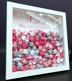 a white frame filled with pink and grey bows on top of a black table next to a bottle