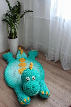 a crocheted stuffed animal laying on the floor next to a potted plant