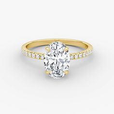 a yellow gold engagement ring with an oval cut diamond in the center and pave set shoulders