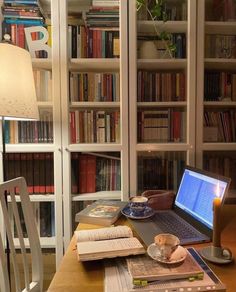 an open laptop computer sitting on top of a wooden desk next to a book shelf