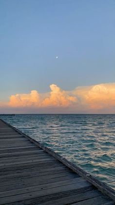 a long pier stretching out into the ocean at sunset with clouds in the sky above