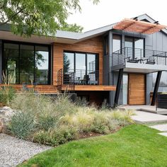 a modern house with wood siding and glass windows on the second floor is surrounded by greenery