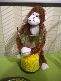 a stuffed monkey sitting inside of a glass vase filled with yellow rice krispy kreme