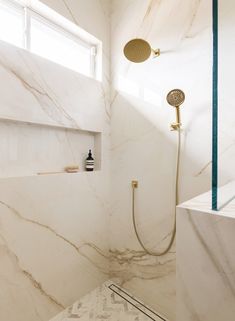 a bathroom with white marble walls and floor, shower head, and hand held faucet