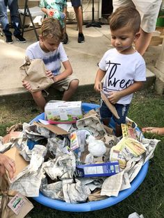 two young boys playing in a trash can filled with paper towels and other garbage bags