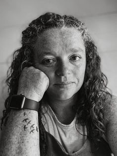 a black and white photo of a woman with tattoos on her arm, looking at the camera