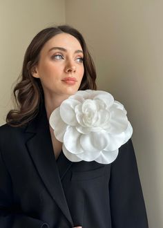 a woman wearing a black suit and white flower brooch