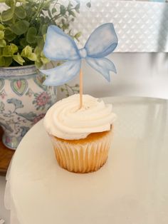 a cupcake with white frosting and a blue bow on top sitting on a table