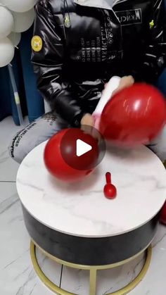 a man in black jacket sitting on top of a table next to balloons and a red balloon