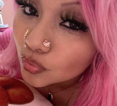 a woman with pink hair and piercings holding a donut