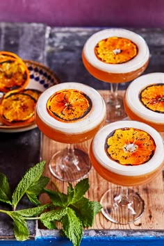 four glasses filled with drinks sitting on top of a wooden tray next to some mint leaves