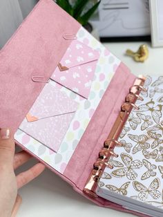 a person is holding a pink binder in front of an open planner book on a desk