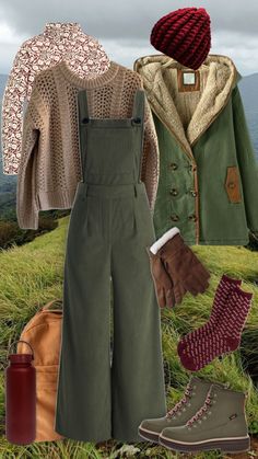 an image of clothes and accessories on the grass with mountains in the background, including boots, sweaters, jacket, gloves, and mittens