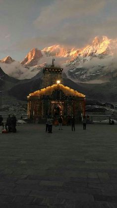 people are standing around in front of a building with lights on it and mountains in the background