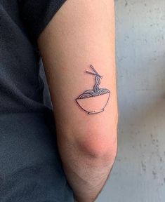 a person with a tattoo on their arm has a bowl of noodles and a spoon in it