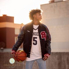 a young man holding a basketball standing in front of a building with his hands on his hips