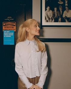 a woman is standing in front of a wall with pictures on it and holding her hands behind her back