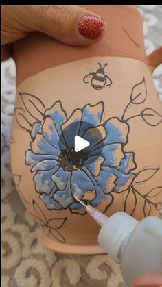 someone is painting a vase with flowers on it and using a marker to paint the flower