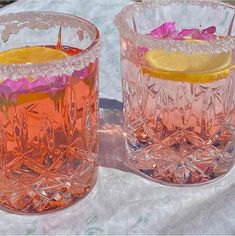 two glasses filled with pink liquid and lemon wedges on top of a white table