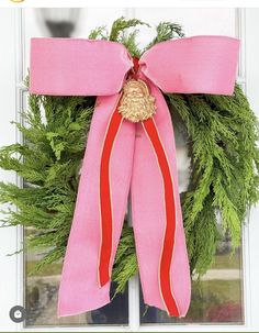 a pink and red christmas wreath hanging on the side of a door with an orange ribbon