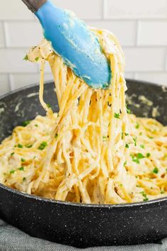 someone using a blue spatula to stir pasta in a skillet with cheese and parsley