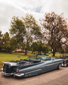 two classic cars parked next to each other on the side of the road with trees in the background