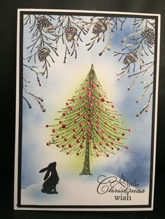 a christmas card with an image of a tree in the snow and a rabbit under it