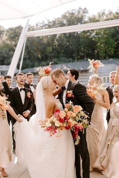 a bride and groom kissing in front of their wedding party