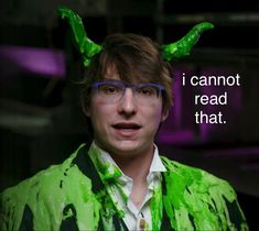 a man with green paint on his face wearing glasses and a green shirt that has horns on it