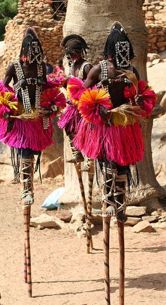 three african dancers in pink and red costumes with headdresses on their heads