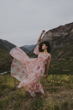 a woman in a long dress is dancing on the grass with her hands up and arms outstretched