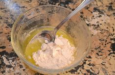 a glass bowl filled with white powder and green liquid next to a spoon on top of a granite counter