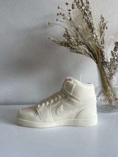 a pair of white sneakers sitting on top of a table next to a vase with dried flowers