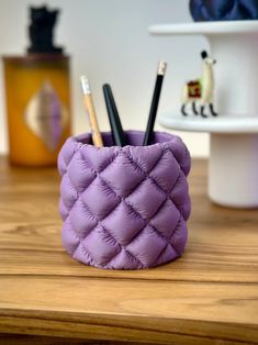 a purple cup sitting on top of a wooden table filled with pens and pencils