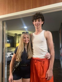 a young man and woman standing next to each other in front of a mirror with their arms around each other