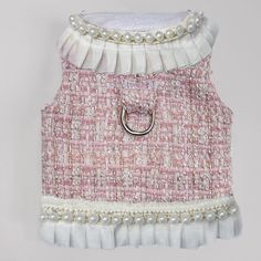 a pink and white dress with pearls on the collar, hanging from a hook in front of a wall