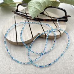 Dainty and bohemian eyeglass necklace chain made with tiny Preciosa Czech crystal seed beads in blue tones and small round faceted cubic zirconia crystals.   Paired with beautiful blue cz gems, this handmade eyeglass chain will definitely create a unique look. This eyeglass lanyard is made on strong quality beading wire with silver plated wire guardians that protect the eyeglass holder grips. The necklace is ended with spring clasps that hold the eyeglass grips and they can be easily removed to Adjustable Blue Glasses Chains With Colorful Beads, Adjustable Glass Beaded Necklaces With Tiny Beads, Beaded Clear Glass Glasses Chains, Adjustable Glass Beaded Necklace With Tiny Beads, Glass Bead Necklaces For Beach, Glass Necklaces With Tiny Beads For The Beach, Adjustable Tiny Beaded Glass Necklaces, Clear Beaded Glass Glasses Chains, Adjustable Tiny Beaded Glass Necklace